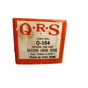 Könnte beinhalten: Eine Vintage QRS Word Roll Box in Orange und Weiß. Die Box zeigt den Text "QRS", "Q-164", "Second Hand Rose" und "Played by Victor Arden". Die Box stammt aus "Follies of 1921".