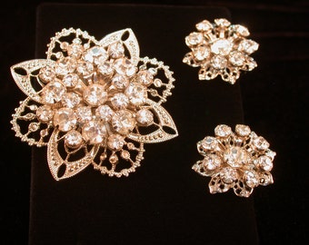 Può includere: Tre spille d'argento con un design floreale e strass trasparenti. La spilla più grande è al centro e le due più piccole sono ai lati.