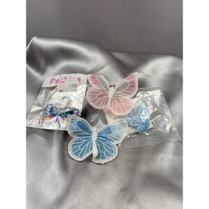 Könnte beinhalten: Drei durchsichtige Schmetterlingsapplikationen in Rosa, Blau und Mehrfarbig. Die Schmetterlinge sind auf einer weißen Karte mit dem Text "Fashion 1200" verpackt.