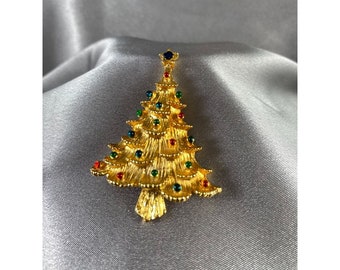 May include: Gold-tone Christmas tree brooch with red, green, and blue jewel accents.