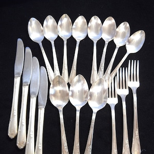 May include: A set of silverware, including spoons, forks, and knives, all made of silver. The silverware is arranged in a symmetrical pattern on a black surface.