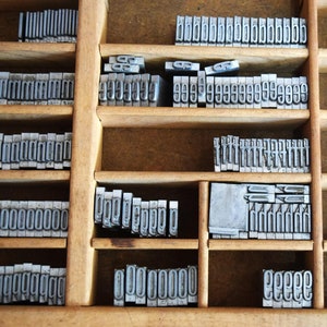 May include: A wooden printing block with metal type in individual compartments. The compartments are labeled with numbers from 0 to 9. The block is filled with various numbers and letters.