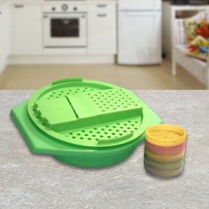May include: A green plastic grater with a removable bowl and a set of colorful plastic containers. The grater has a variety of holes and blades for grating different types of food.