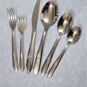 May include: Set of five silver-toned flatware pieces, including a knife, fork, and three spoons. The pieces have a floral design.