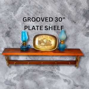 May include: A 30-inch grooved wooden shelf with brass hooks and a decorative brass plate with a religious inscription. Two blue glass oil lamps are on the shelf.