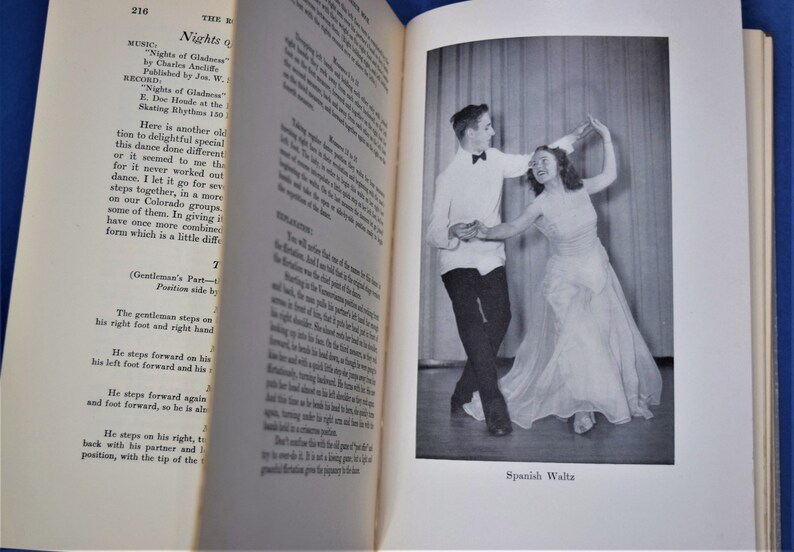 May include: A black and white photograph of a couple dancing the Spanish Waltz. The man is wearing a white shirt with a black bow tie and black pants. The woman is wearing a white dress. The caption below the photo reads "Spanish Waltz."