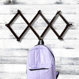 May include: A lavender quilted backpack hanging on a wooden wall rack with six hooks. The rack is in a diamond pattern.
