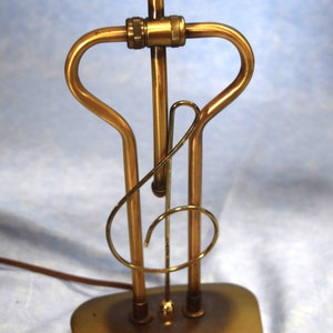 K&ouml;nnte beinhalten: Eine goldfarbene Tischlampe mit einem einzigartigen Design in Form eines Violinschl&uuml;ssels. Die Lampe hat einen runden Sockel und einen schlanken, gebogenen Schaft.