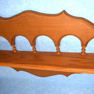 May include: A wooden shelf with a decorative arched top and five decorative spindles. The shelf is stained a medium brown color.