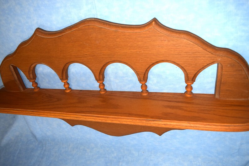 May include: A wooden shelf with a decorative arched top and five decorative spindles. The shelf is stained a medium brown color.