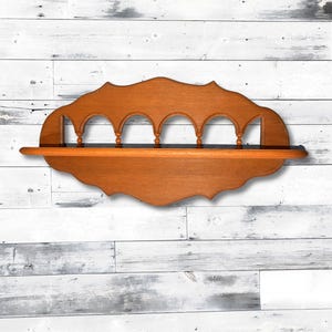 May include: A wooden shelf with a decorative, scalloped edge and five arched openings. The shelf is stained a rich brown color.