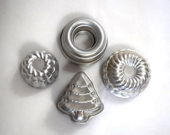 May include: Four silver metal cake molds in different shapes: a ring, a wreath, a tree, and a round mold with a fluted edge.