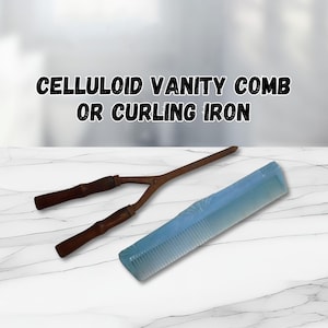 May include: A vintage curling iron and a light blue celluloid comb rest on a white marble surface. The curling iron has a Y-shaped design with wooden handles. The comb is rectangular with a decorative pattern.