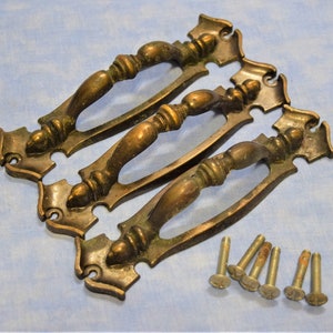 May include: Three antique brass drawer pulls with ornate designs and a set of screws.