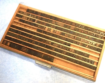 May include: A wooden drawer filled with rows of vintage metal letterpress printing blocks. The blocks are arranged in alphabetical order and include both uppercase and lowercase letters, numbers, and punctuation marks.