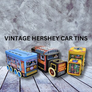 May include: Three vintage tin toy cars, each with a different design. The first car is blue and white with the text "Hershey's Transit Co." The second car is black and red with the text "Hershey Chocolate Company." The third car is yellow and red with a monkey and the text "Hershey Chocolate Company."