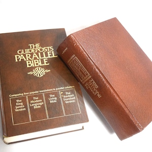 May include: Two brown leather-bound Bibles. One is open, displaying the title "The Guideposts Parallel Bible" in gold lettering. The other is closed, with the title visible on the spine. The books compare four popular Bible translations.