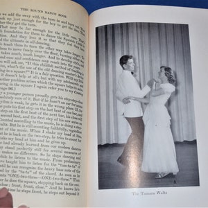 May include: A black and white photograph of a couple dancing the Tamara Waltz. The man is wearing a white shirt and black pants. The woman is wearing a white dress. The couple is dancing in front of a white curtain.