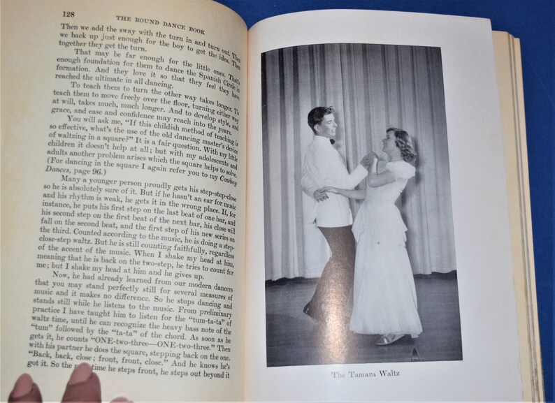 May include: A black and white photograph of a couple dancing the Tamara Waltz. The man is wearing a white shirt and black pants. The woman is wearing a white dress. The couple is dancing in front of a white curtain.