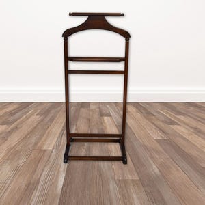 May include: A dark brown wooden valet stand featuring a contoured coat hanger top, a horizontal bar for trousers, and a small shelf for accessories. The structure is supported by a rectangular base, providing a stable frame for organizing clothing items.