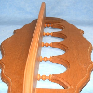 May include: A wooden shelf with a decorative scalloped edge and five decorative wooden knobs. The shelf is stained a light brown color.