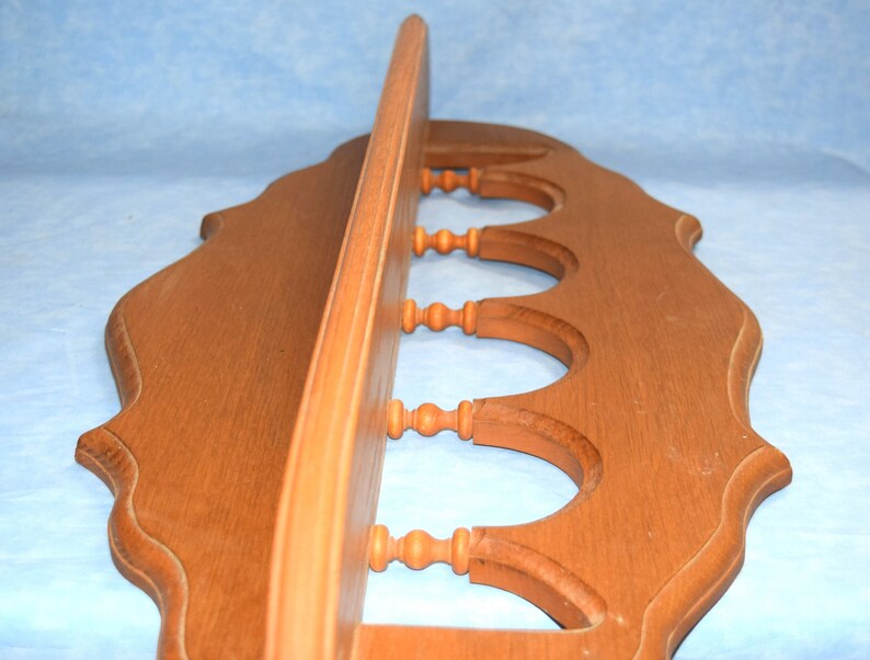 May include: A wooden shelf with a decorative scalloped edge and five decorative wooden knobs. The shelf is stained a light brown color.