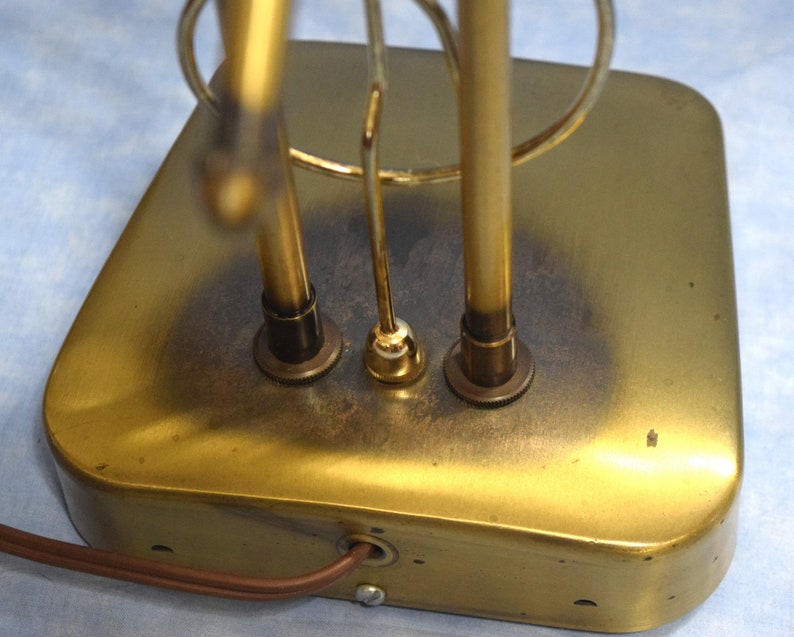K&ouml;nnte beinhalten: Ein goldfarbener Metall-Tischlampenfu&szlig; mit einem runden Design und drei Stromkabeln. Die Basis hat eine abgenutzte, gealterte Oberfl&auml;che.