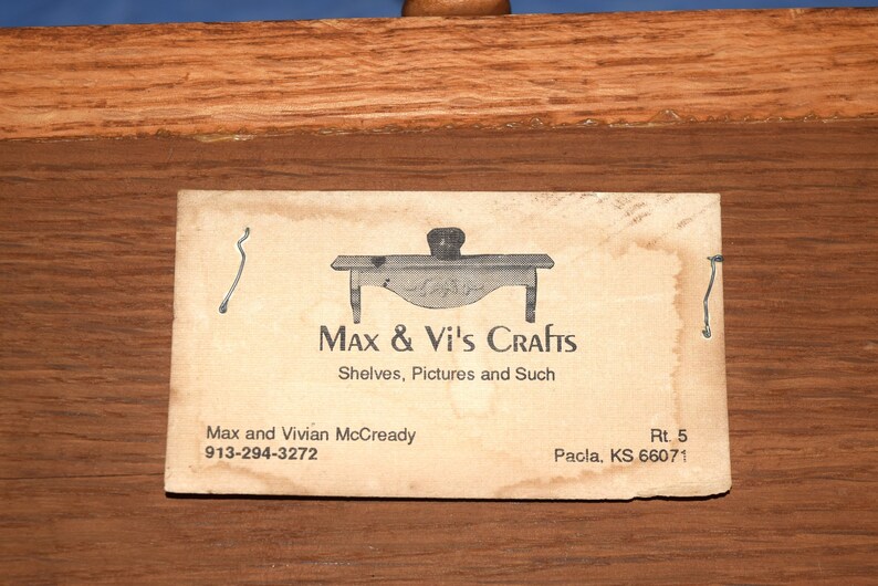 May include: A business card for Max & Vi's Crafts, which specializes in shelves, pictures, and other crafts. The card features a small illustration of a table and the text "Max & Vi's Crafts, Shelves, Pictures and Such, Max and Vivian McCready, 913-294-3272, Rt. 5, Pacla, KS 66071."