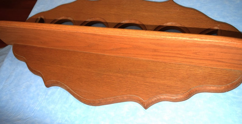 May include: A wooden wall shelf with a scalloped edge and five round cutouts. The shelf is stained a rich brown color.