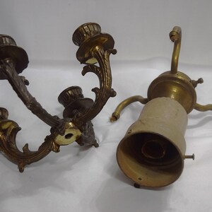 May include: Two antique brass candle holders, one with three arms and the other with a single arm. Both have ornate designs and are in good condition.