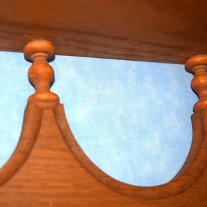 May include: Close-up of a wooden shelf with two decorative finials. The finials are brown and have a rounded shape. The shelf is against a light blue background.