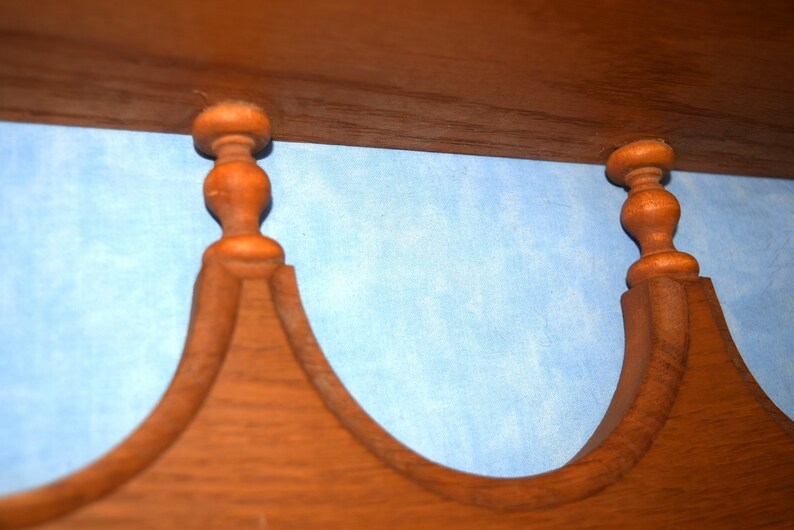 May include: Close-up of a wooden shelf with two decorative finials. The finials are brown and have a rounded shape. The shelf is against a light blue background.