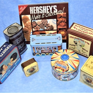 May include: A collection of vintage Hershey's chocolate tins, including a cocoa tin, a milk chocolate tin, a Kisses tin, a tin with a carousel design, a tin shaped like a trolley car, and a tin with a 1990 calendar featuring Hershey's chocolate recipes.