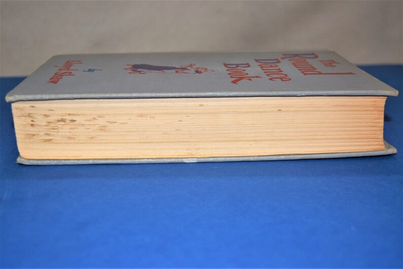 May include: The Round Dance Book by  Eleanor  Selfridge. The book has a blue cover with a red title and a black and white illustration of a couple dancing.