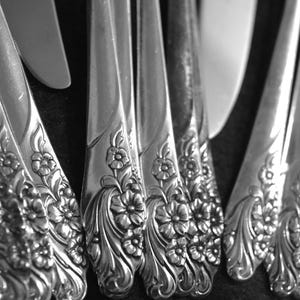 May include: A set of silver flatware with ornate floral designs. The handles are intricately detailed with a repeating pattern of flowers and leaves.