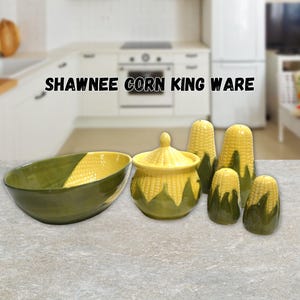 May include: A collection of Shawnee Corn King Ware ceramic kitchen items including a large oval bowl, a lidded sugar bowl, and four shakers, all featuring a yellow corn kernel pattern with green husks at the base and on the exterior surfaces.