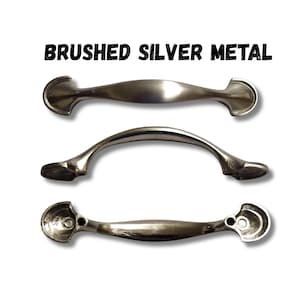 May include: Three brushed silver metal cabinet pulls arranged vertically. The top pull is viewed from the front, the middle pull is arched, and the bottom pull shows the back side with two circular mounting holes on each end. Text reads BRUSHED SILVER METAL.