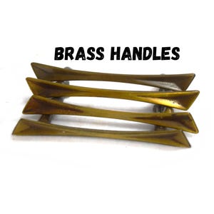May include: Four brass handles are stacked on a white background. The handles are a warm brass color with a slightly curved design. The text "BRASS HANDLES" is printed in bold black letters above the handles.