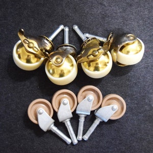 May include: A collection of furniture casters. The top row features gold-toned metal casters with ivory-colored wheels. The bottom row shows brown casters with silver-toned metal stems. The casters are designed for furniture.