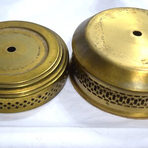 May include: Two round, gold-colored metal cake stands with decorative cutouts around the edges. The smaller stand has a solid top, while the larger stand has a slightly raised, solid top.