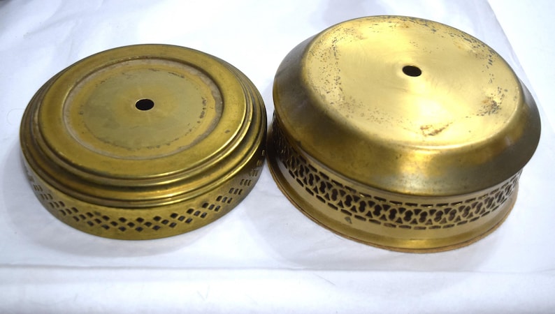 May include: Two round, gold-colored metal cake stands with decorative cutouts around the edges. The smaller stand has a solid top, while the larger stand has a slightly raised, solid top.