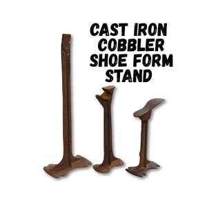 May include: Three cast iron cobbler shoe form stands. The stands are brown and have a rustic appearance. The text "CAST IRON COBBLER SHOE FORM STAND" is in black above the stands.