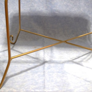 May include: Gold metal table base with a criss-cross design and curled feet.