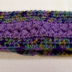 May include: A purple, green, and brown knitted headband. The headband is made of a soft, textured yarn.