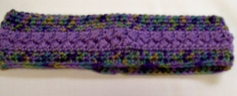 May include: A purple, green, and brown knitted headband. The headband is made of a soft, textured yarn.