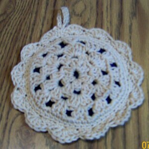 May include: A crocheted beige pot holder with a circular design. The pot holder has a loop for hanging.