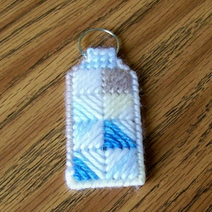 May include: A blue, white, and brown key chain with a geometric pattern. The key chain is made of plastic canvas and has a metal ring.