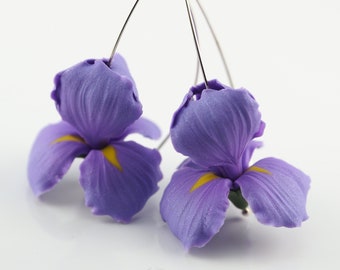May include: A pair of purple iris flower earrings with silver wire hooks. The flowers have yellow centers.