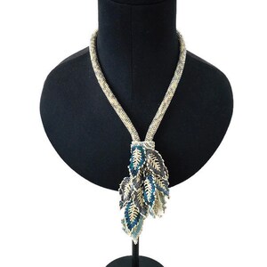 May include: A long, beaded necklace with a pendant made of multiple blue, white, and gray leaves. The necklace is displayed on a black mannequin.