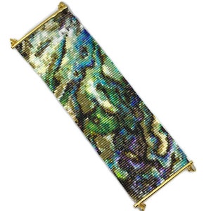 K&ouml;nnte beinhalten: Ein Armband aus Perlen mit einem farbenfrohen, abstrakten Muster. Das Armband besteht aus kleinen, schillernden Perlen und hat einen goldenen Verschluss.
